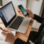 Pessoa com celular e notebook. Respostas Automáticas no WhatsApp Business – Como Configurar